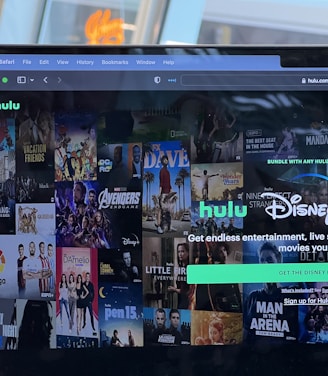 A laptop screen displays a web page featuring a mix of movie and TV show covers, highlighting popular titles and a Hulu and Disney+ bundle promotion. There are visible icons and images of films and shows alongside promotional text offering entertainment and live sports.